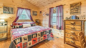 Ein gemütliches Schlafzimmer in einer Blockhütte mit einem gesteppten Bett, einer Holzkommode und einem Fenster mit Vorhängen.