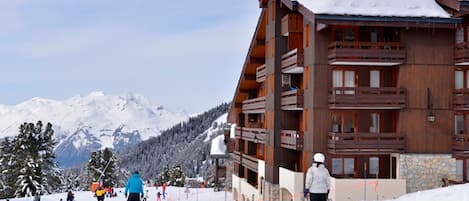 A ski resort building with multiple balconies and a stone facade, surrounded by snow-covered mountains.