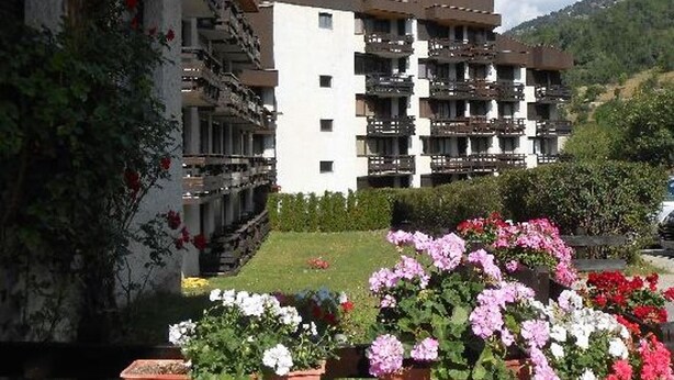 A multi-story building with balconies, surrounded by a well-maintained garden with various flowers.