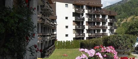 Un edificio de varios pisos con balcones, rodeado por un jardín cuidado con diversas flores.