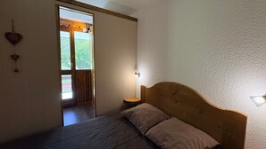 A bedroom with a wooden bed, a window with curtains, and a view of greenery outside.
