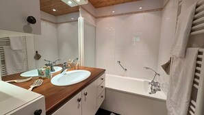 A modern bathroom with two sinks, a bathtub, and a wooden ceiling.