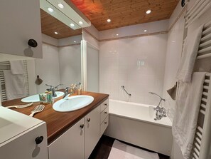 Un baño moderno con dos lavamanos, una bañera y techo de madera.