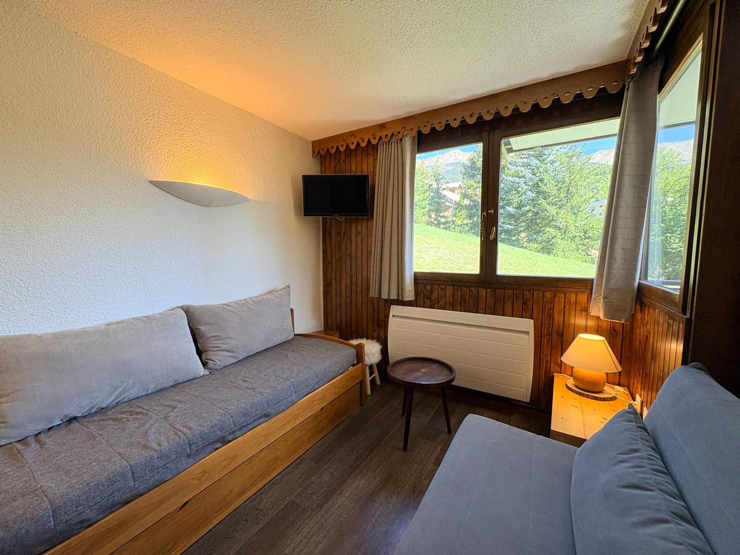 Une pièce comprenant un canapé, une petite table avec une lampe, un téléviseur et une fenêtre avec des rideaux.