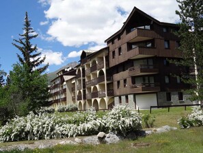 A multi-story hotel with balconies and a garden with white flowering bushes.