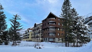 A multi-story hotel with balconies, surrounded by snow-covered trees and a mountainous backdrop. - Cozy studio with slopes access, shuttle and parking. For 4 guests. (La Salle-les-Alpes)