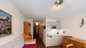 A compact room with a bed, a wooden desk, a kitchenette, and a hallway leading to another room. - Cozy studio with slopes access, shuttle and parking. For 4 guests. (La Salle-les-Alpes)