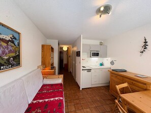 Una camera compatta con un letto, una scrivania in legno, un angolo cottura e un corridoio che porta a un'altra stanza.