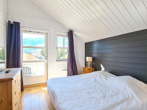 A bedroom with a bed, a dresser, a nightstand with a lamp, and a window with curtains.