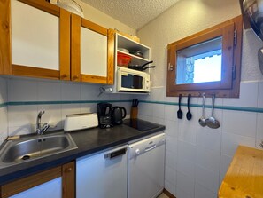 A compact kitchen with wooden cabinets, a microwave, a dishwasher, and a window with a view.