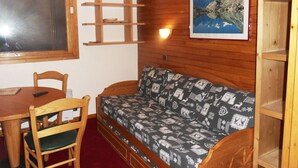 A cozy room with a wooden wall, a sofa with a patterned cover, a wooden table with chairs, and a framed picture on the wall. - Functional studio at the foot of the slopes for 3/4 people, balcony, divisible living (Belle Plagne)