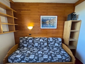 A cozy room with a wooden wall, a framed picture, a wall-mounted light, and a wooden shelf.