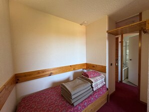 A small, single-bed room with a wooden headboard, a patterned bedspread, and a red carpeted floor.