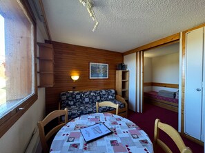 A cozy room with a round table, a sofa, a wooden wall, a ceiling fan, and a bed with a red blanket.