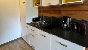 Una cocina compacta con armarios blancos, encimera negra y paneles de madera en la pared.