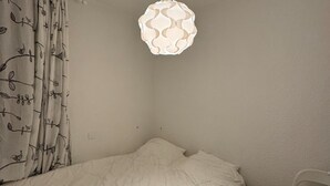 Una cama individual con un edredón blanco en una habitación con una pared blanca lisa y un colgante de luz.