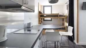 Une cuisine compacte au design moderne, comprenant une hotte en acier inoxydable, un four encastré et un petit coin repas avec une table ronde et des chaises blanches.