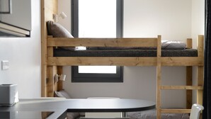 Une chambre avec un lit superposé, un bureau et une chaise, une fenêtre et une petite table.