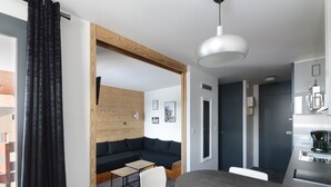 Un espace de vie moderne avec un canapé gris foncé, un mur d’accent en bois, un coin repas avec une table grise et une cuisine équipée d’une machine à café.