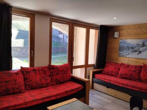 A room with two red sofas, a wooden table, and a painting of a snowy landscape on the wall. - Renovated 2-room apartment, near slopes, balcony, pets allowed (La Plagne Montchavin Les Coches)