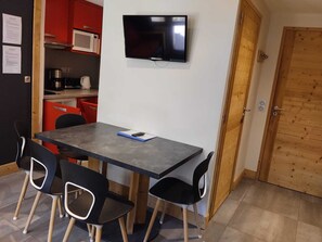 A compact room with a dining table, four chairs, a television mounted on the wall, and a wooden door. - Renovated 2-room apartment, near slopes, balcony, pets allowed (La Plagne Montchavin Les Coches)
