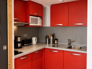 Une cuisine de taille réduite avec des meubles de rangement rouges, un four à micro-ondes, une machine à café et un évier.