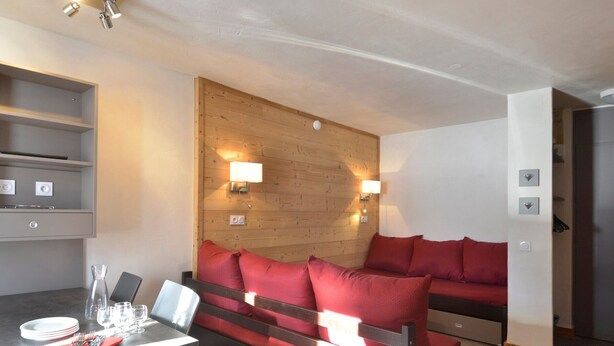 A modern room with a wooden accent wall, a sofa, a dining table set with plates and glasses, and a wall-mounted light fixture.