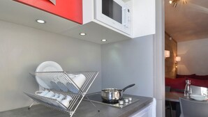 A compact kitchen with a microwave, a dish rack, a sink, and a dining area with red seating.