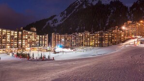 A snow-covered ski resort at night with illuminated buildings and a mountain in the background.