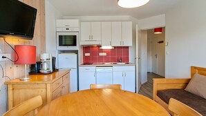 A compact kitchen with white cabinets, a red backsplash, a coffee machine, and a TV mounted on the wall. - Bright apartment in center with balcony and parking (Flaine)
