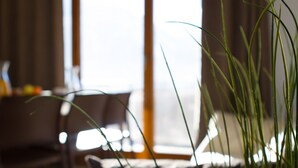 Una habitación con un ventanal grande, un comedor con mesa y sillas, y una planta al frente.