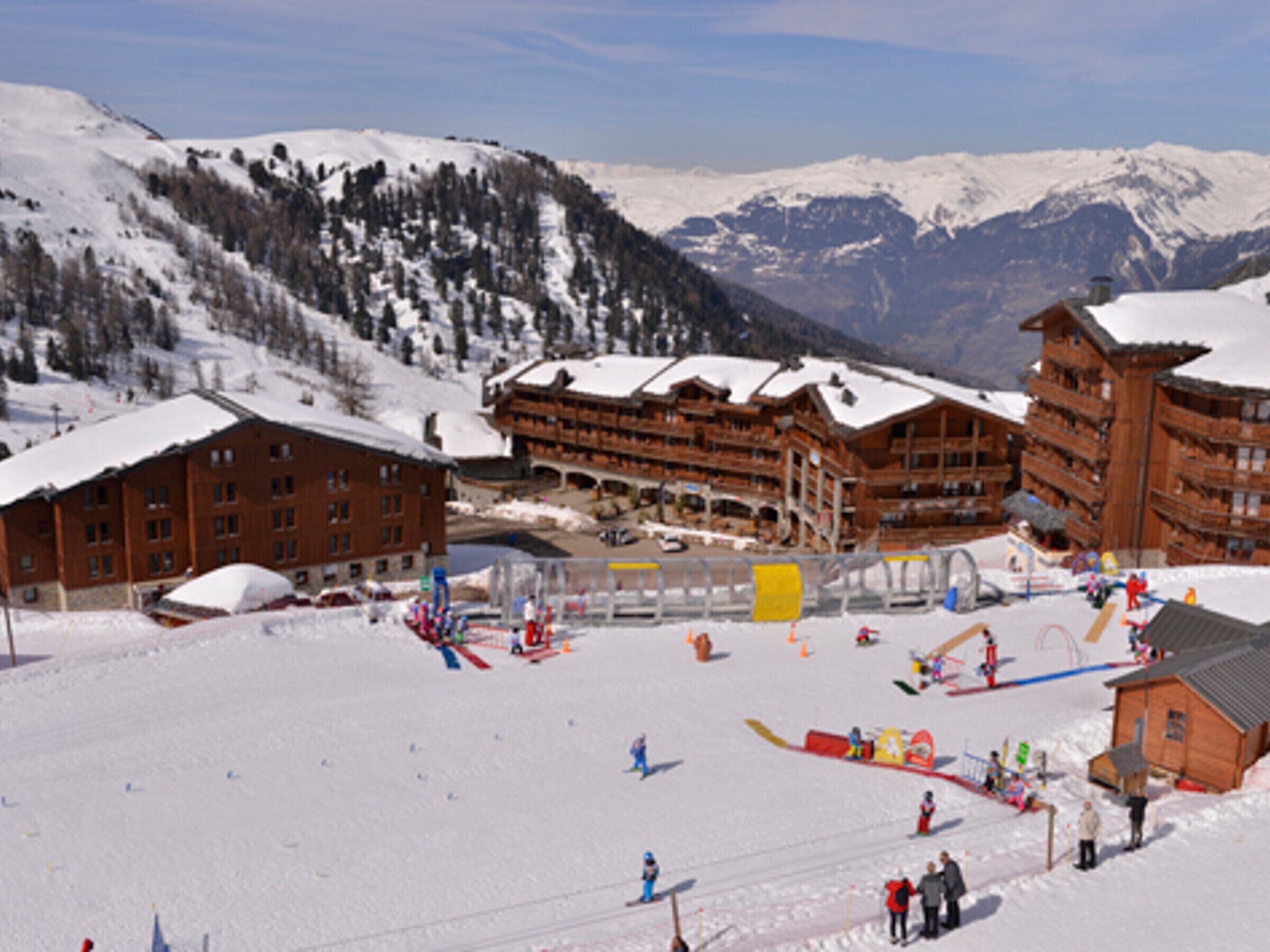 Une station de ski comprenant plusieurs bâtiments en bois, un télésiège et un paysage montagneux enneigé en toile de fond.