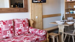 Et hyggeligt værelse med en træsofa, et fjernsyn ophængt på væggen, et træbord med tallerkener og et spejl over sofaen.