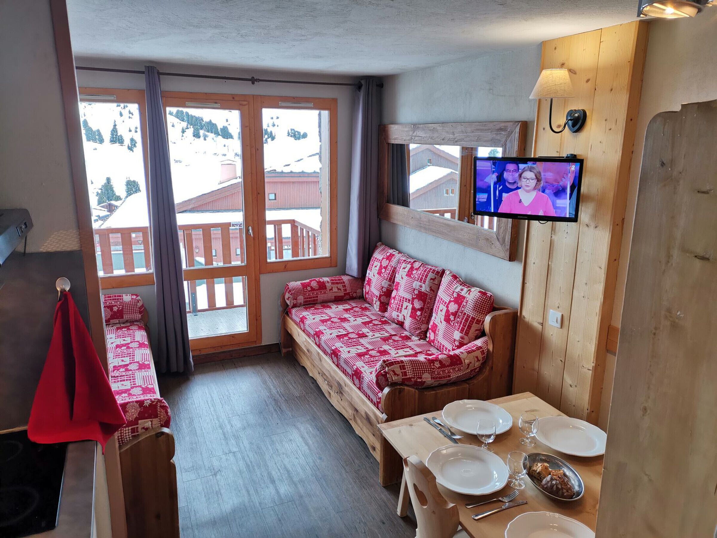 Ein gemütliches Zimmer mit einer Holz-Couch, einem Esstisch für zwei Personen und einem an der Wand montierten Fernseher.
