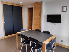 A conference room with a long table, four chairs, a television on the wall, and a wooden partition.