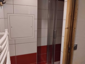 Ein Badezimmer mit Duschkabine, einer weißen Fliesenwand mit rotem Sockel und einer Tür mit Holzrahmen.