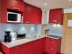 A compact kitchen with red cabinets, a microwave, a coffee maker, a toaster, and a sink.