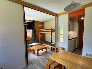 Habitación pequeña con literas, una mesita y un rincón americano.