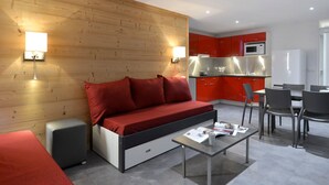 Ein modernes Wohnzimmer mit einer Couch, einem Couchtisch und einer Küchenzeile mit roten Schränken und einer Mikrowelle.