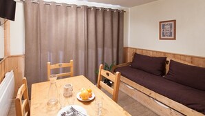 A cozy room with a wooden table set for dining, a sofa, and a television. - Comfortable studio near slopes, Free Wifi, Pets allowed (Briançon)