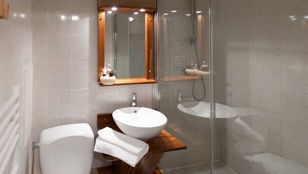 A modern bathroom with a glass-enclosed shower, a wooden vanity, and a white toilet.