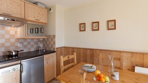 A compact kitchen with wooden cabinets, a built-in oven, and a dining area with a wooden table set for four. - Comfortable studio near slopes, Free Wifi, Pets allowed (Briançon)