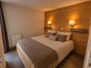 A bedroom with a wooden headboard, two bedside lamps, a bed with a blanket, and a radiator.