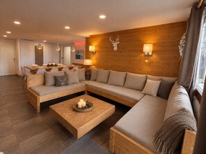 A modern living room with a wooden sofa, a coffee table, and a dining area with chairs and a table.
