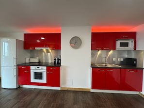 A kitchen with red cabinets, a white refrigerator, a microwave, and a clock on the wall.