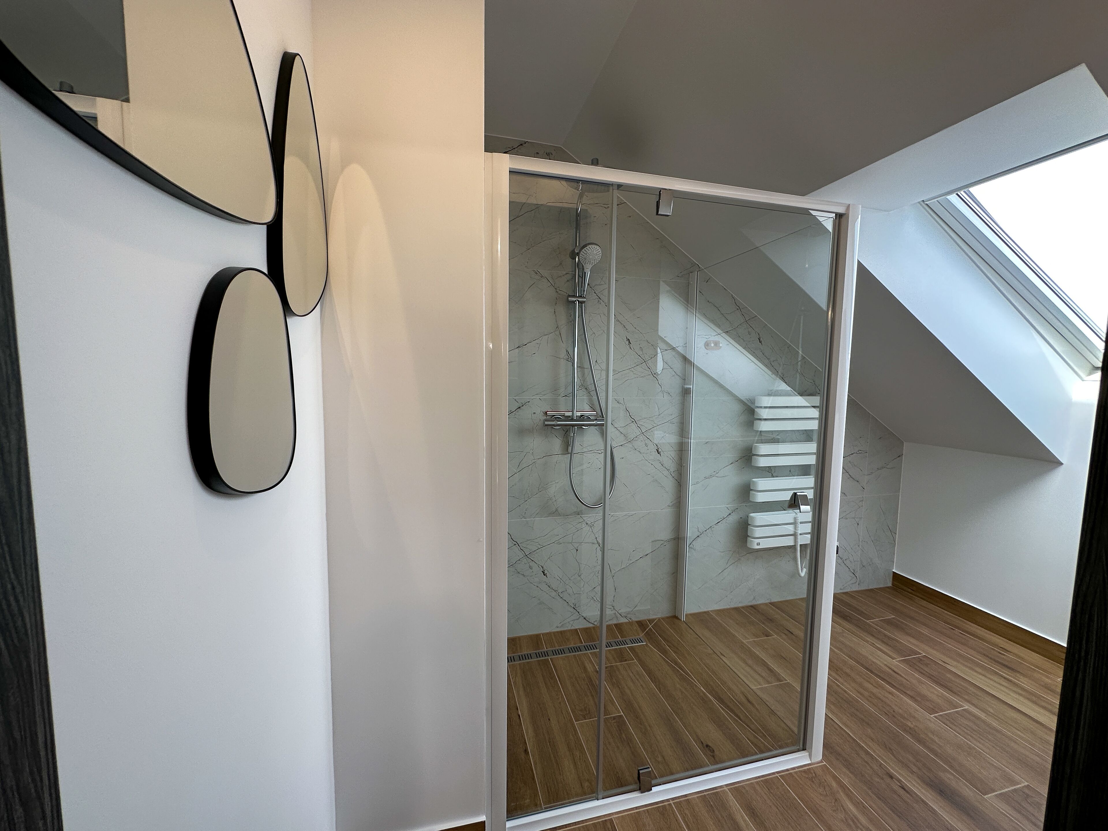 A modern bathroom with a glass shower enclosure, a wooden floor, and a skylight.