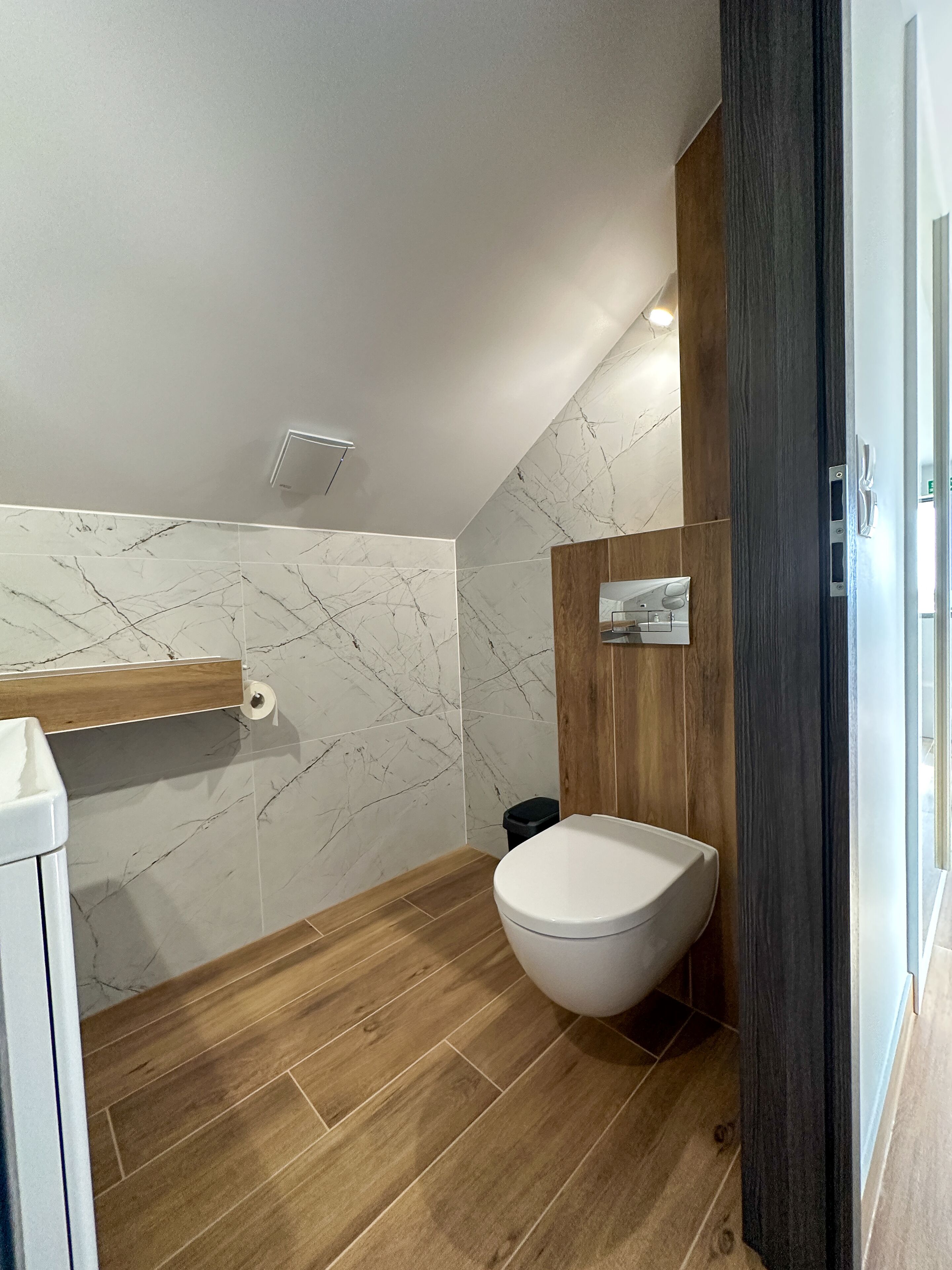 Ein modernes Badezimmer mit Toilette in Weiß, Holzboden und Marmorwänden.