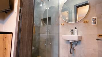 A modern bathroom with a glass shower enclosure, a round mirror, a white sink, and a toilet.