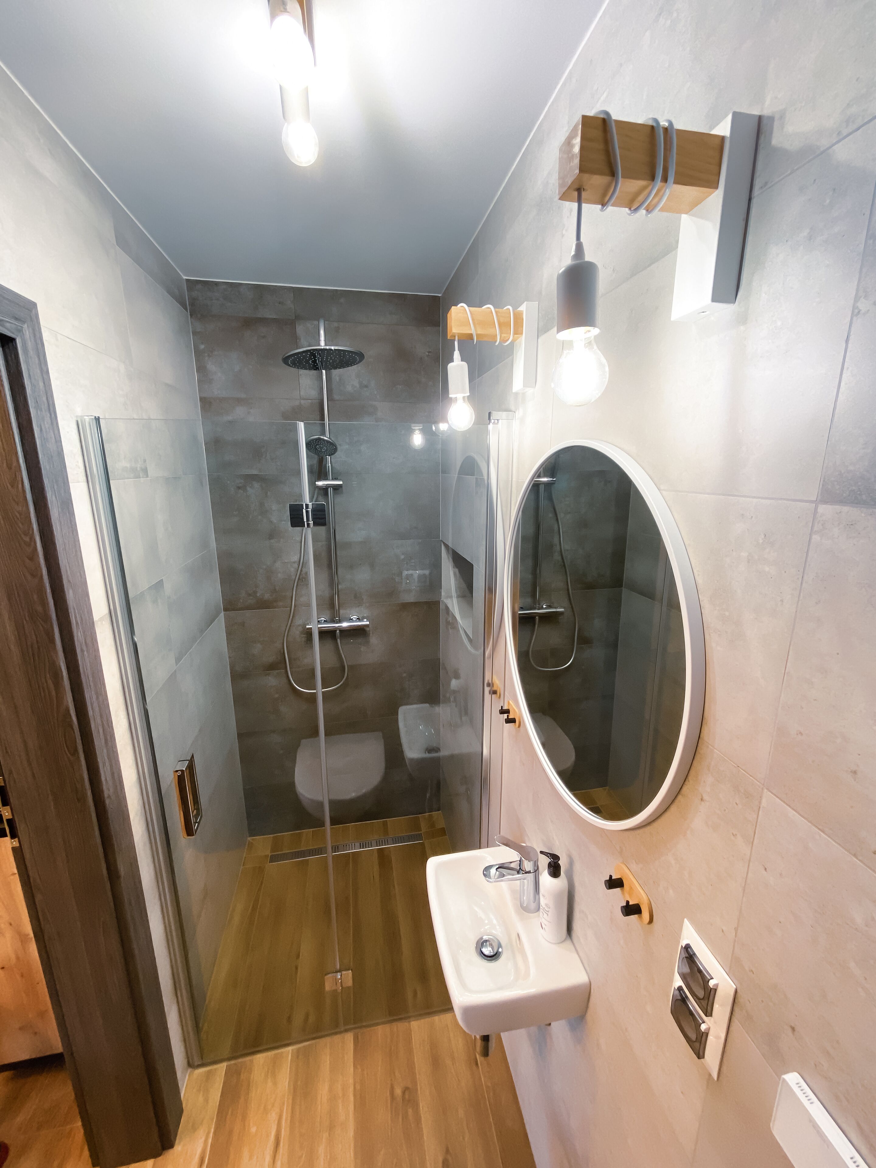 A modern bathroom with a glass-enclosed shower, a round mirror, and a wooden vanity.