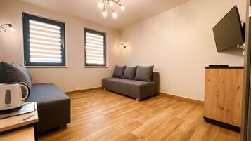 Een moderne woonkamer met een grijze bank, een houten salontafel en een flatscreen televisie aan de muur.
